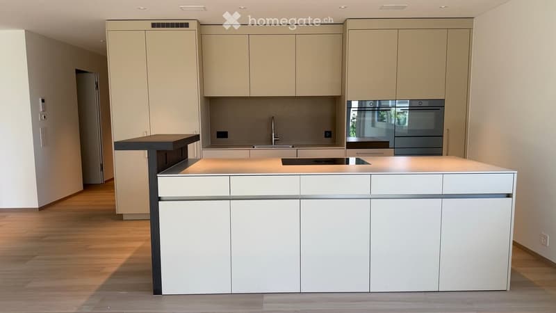 Modern kitchen with a white and beige color scheme, featuring a central island with built-in cabinets, a sink, and an oven.