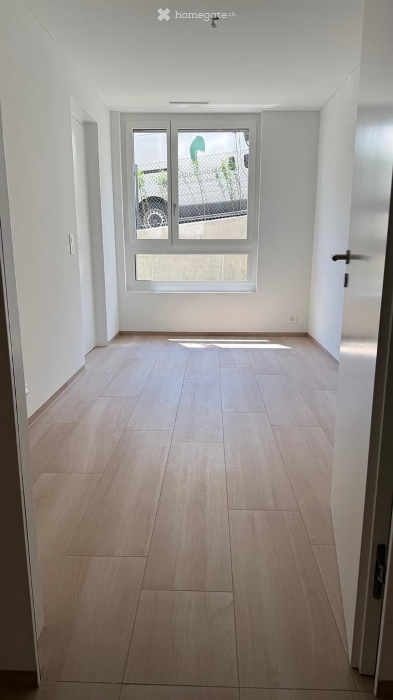 Empty hallway with light wooden flooring, white walls, and a large window at the end.