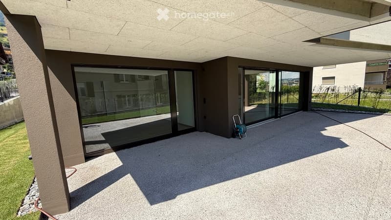 Modern covered balcony with large glass sliding doors, concrete floor, and a view of the surrounding area.
