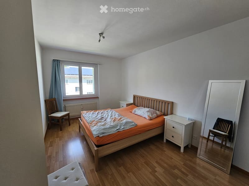 Cozy bedroom with wooden flooring, a single bed with orange bedding, a nightstand, a chair, a mirror, and a small stool.