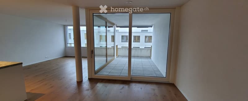 Empty room with wooden flooring, large glass sliding doors leading to a tiled balcony area.