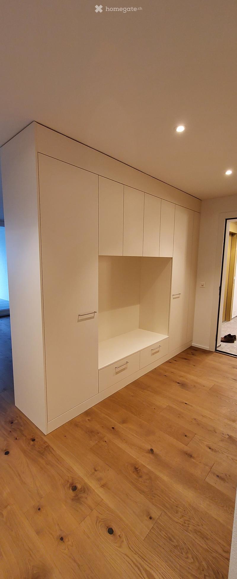 Empty room with light wooden flooring and built-in white storage units featuring drawers and shelves.