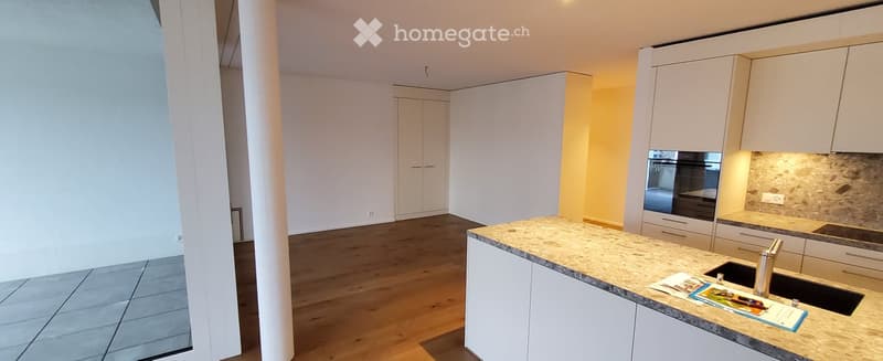 Empty kitchen with white cabinets, granite countertop, sink, and wooden flooring. No appliances or furniture present.