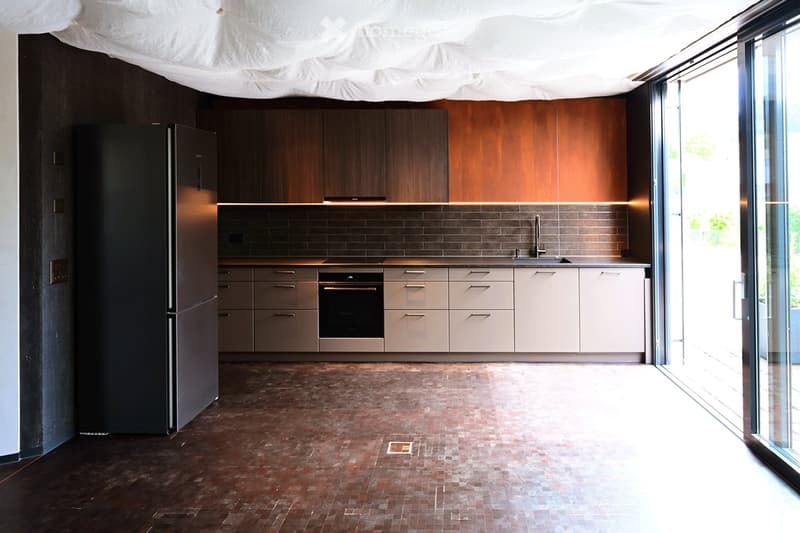 Modern kitchen with dark wooden cabinets, stainless steel appliances, and a large window providing natural light.