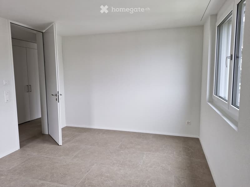 Empty room with light-colored walls, tiled floor, and a large window. A door leads to another room.