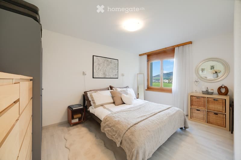 Cozy bedroom with a large bed, nightstand, wicker storage unit, and a scenic window view.