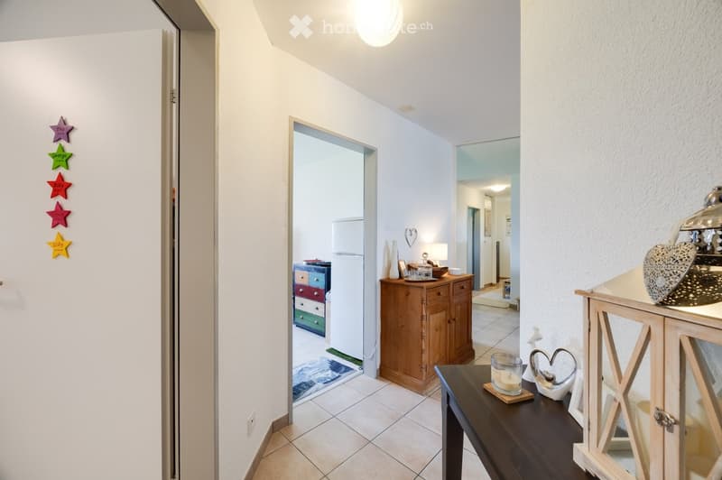 A well-lit hallway with tiled flooring, white walls, and several doors. Visible decorations include colorful star-shaped wall decals and a small wooden side table with a candle and decorative items.