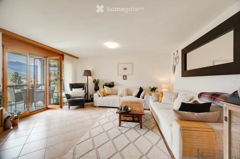 Bright living room with large sliding glass doors leading to a balcony, white sofa, coffee table, armchair, and floor lamp.