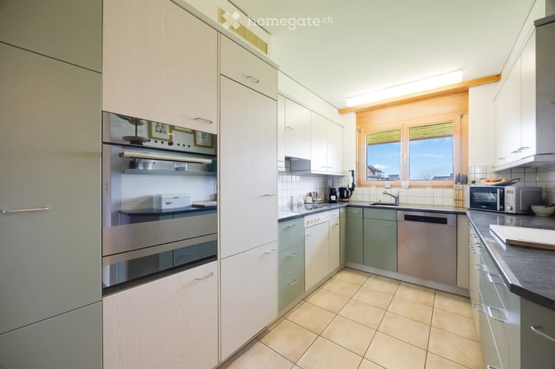 Modern kitchen with light wood cabinets, stainless steel appliances, and a large window offering a view.