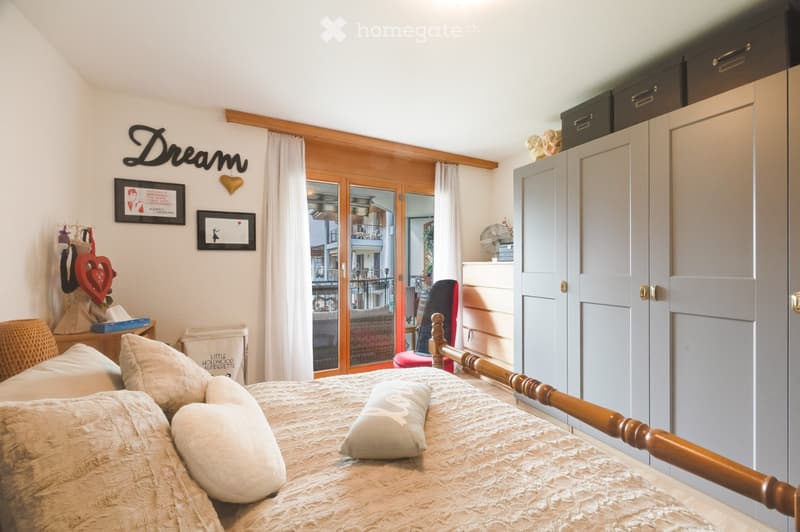Cozy bedroom with a wooden bed frame, soft bedding, nightstand, and a view to a balcony through large glass doors.