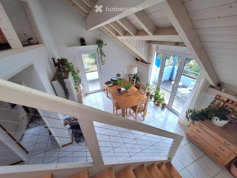 Bright, airy room with wooden beams, white walls, and large windows. Features a dining table with chairs, a lamp, potted plants, and a cabinet with drawers.