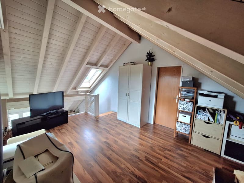 Bright attic room with wooden floors, slanted wooden ceiling, large skylight window, and modern furniture including a sofa, TV, and storage units.