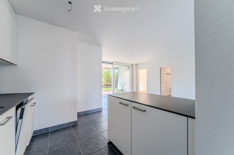 Modern kitchen with white cabinets, dark countertops, and tiled flooring. Features an open layout with a sliding glass door leading to an outdoor area.
