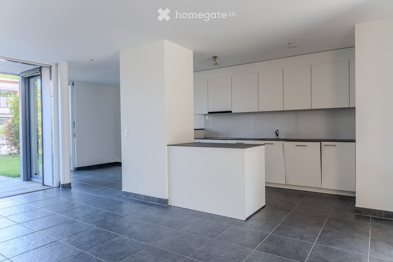 Modern kitchen with white cabinets, a central island, and dark tiled flooring. Large sliding glass door provides access to outdoor area.