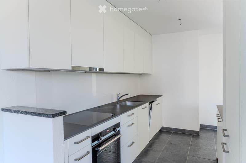 Modern kitchen with white cabinets, black countertops, and stainless steel appliances including a sink, faucet, and oven.