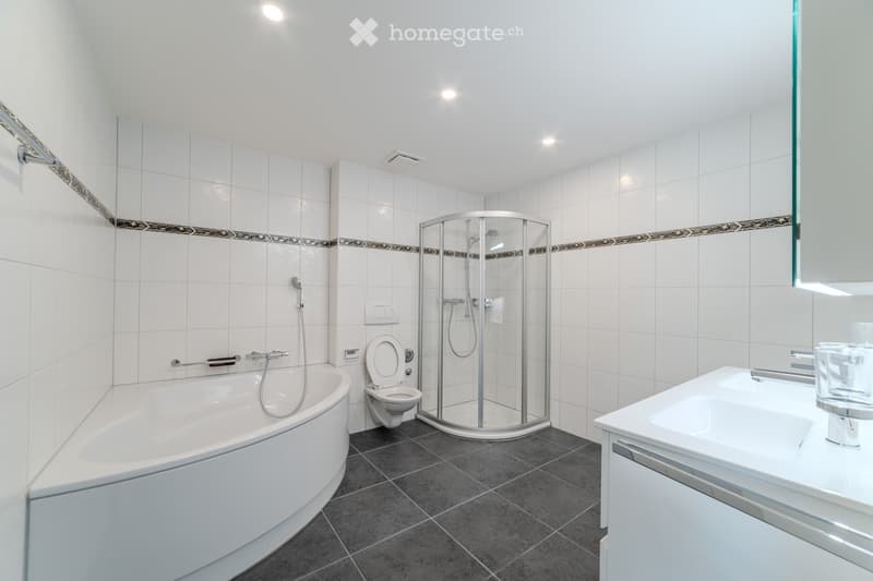 Modern bathroom with white tiles, a bathtub, toilet, glass-enclosed shower, and a sink with a mirror.