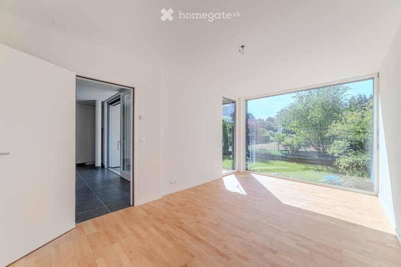 Empty room with light wooden flooring, white walls, large windows, and a door leading to another space.