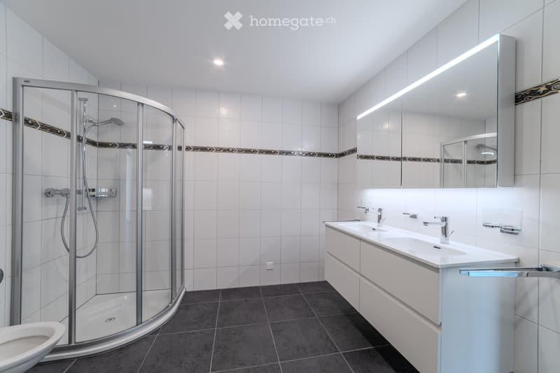 Modern bathroom with white tiles, a glass-enclosed shower, a double sink vanity, and a toilet.