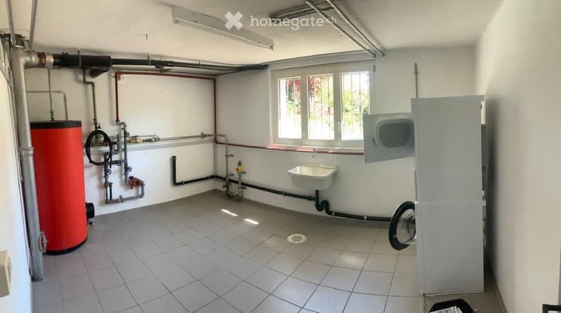 Utility bathroom with tiled floor, white walls, sink, water heater, and air conditioning unit. Windows provide natural light.