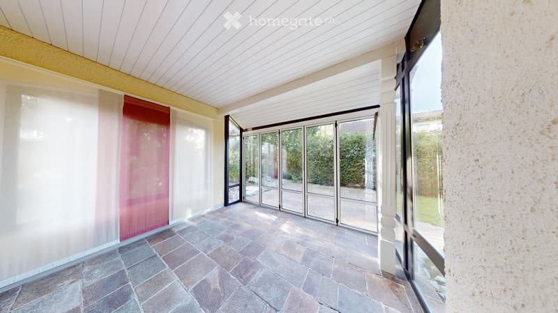 Spacious balcony with tiled flooring, large glass doors, white walls, and a view of the garden.