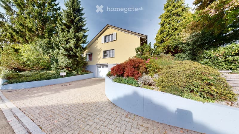 Two-story yellow house with white trim, garage, surrounded by lush greenery and a well-maintained garden.