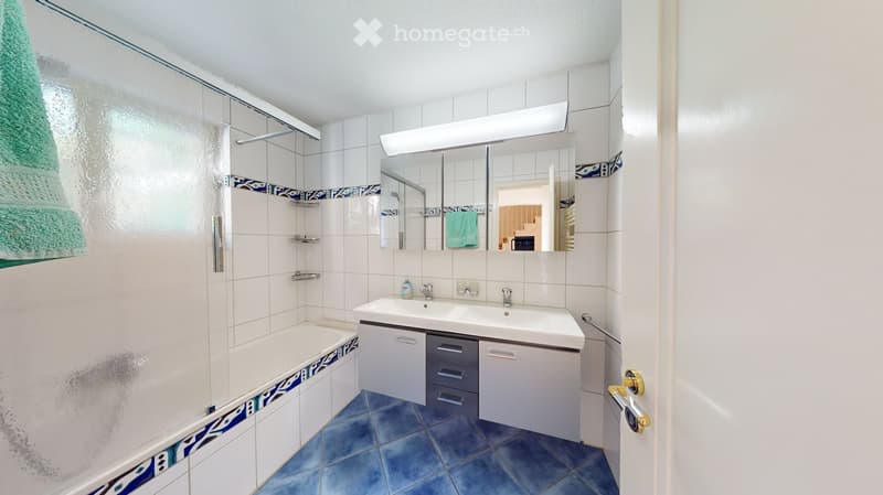 Bathroom with a bathtub, double sink, mirror, and cabinet. Blue tiles on the floor and white tiles on the walls, with a decorative border.