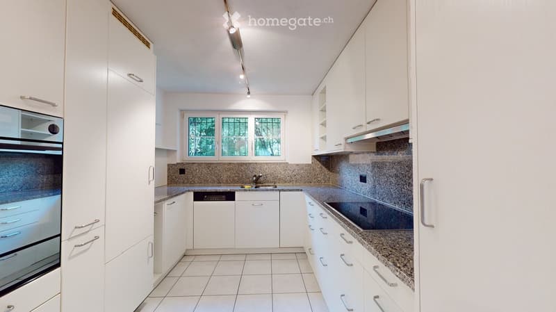 Modern kitchen with white cabinets, granite countertops, and stainless steel appliances including an oven and dishwasher. Features a window above the sink and recessed lighting.