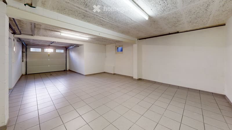Empty garage with tiled floor, white walls, and a large garage door. No furniture or equipment present.