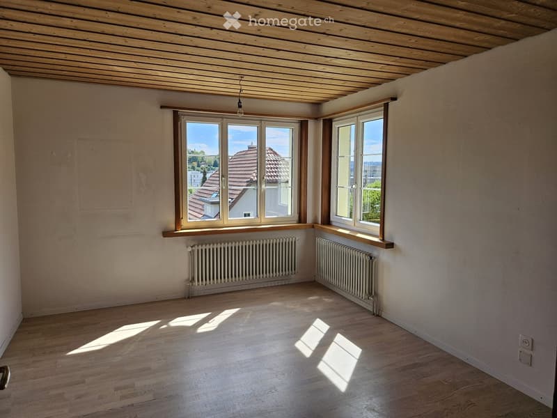 Empty room with wooden flooring, white walls, large windows with wooden frames, radiators, and a wooden ceiling.