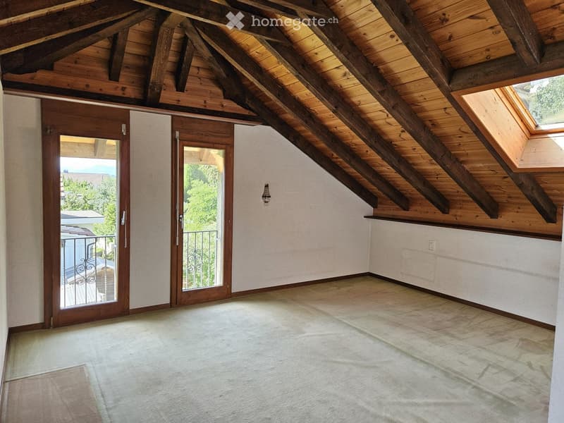 An empty attic space with wooden beams, exposed wooden ceiling, and two wooden doors leading to a balcony area.