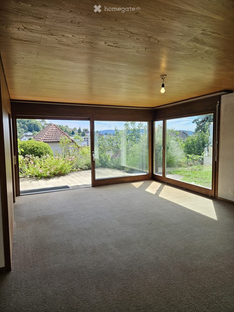 Empty room with carpeted floor, large sliding glass doors leading to a garden, wooden ceiling, and recessed lighting.