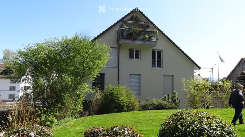 House. Two-story house with a balcony, surrounded by a well-maintained lawn and garden.