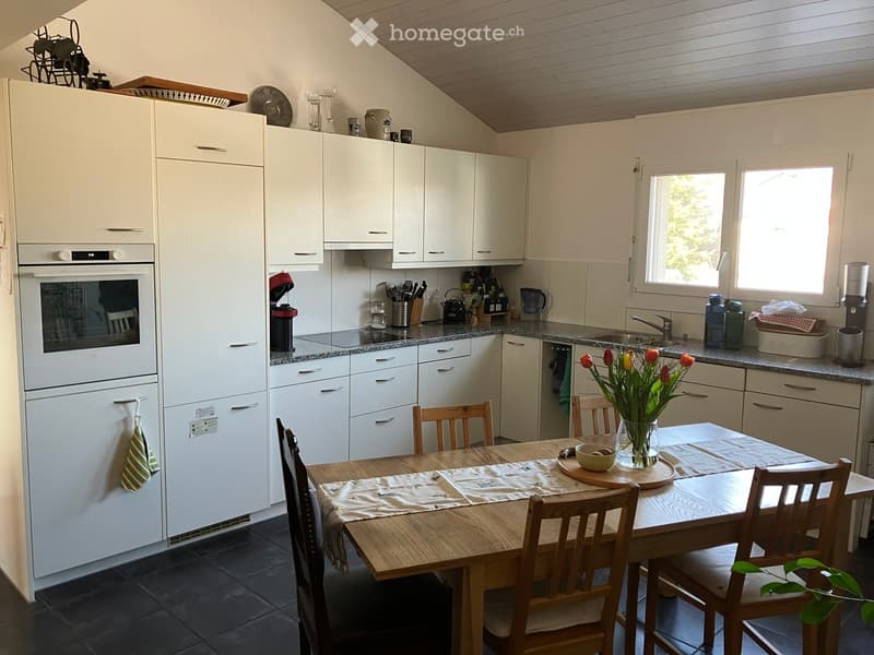 Kitchen. Bright kitchen with white cabinets, granite countertops, and a wooden dining table with chairs. Appliances include a refrigerator, oven, and dishwasher. A vase of tulips is on the table.
