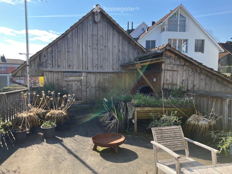 Garden / Outdoor Area. Garden area with wooden chair, fire bowl, and several potted plants near a wooden barn and house.