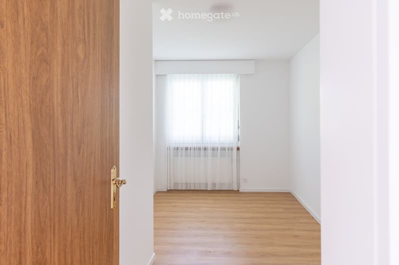 Empty room with wooden flooring, white walls, and a window with sheer curtains. No furniture or equipment is present.