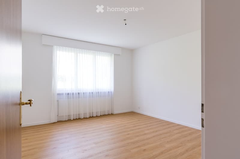 Empty room with wooden flooring, white walls, and a window with sheer curtains. No furniture or equipment present.