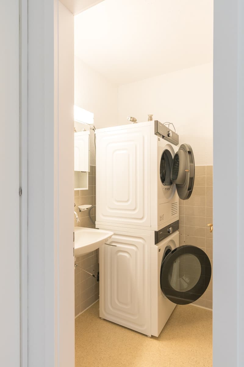 A compact bathroom with a stacked washer and dryer unit, a sink, and tiled walls.