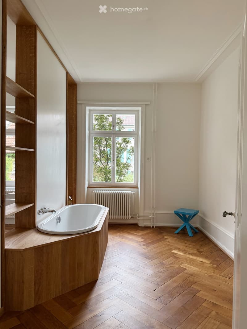 Bathroom with a freestanding bathtub, wooden shelving, a small blue stool, and a radiator under a large window.
