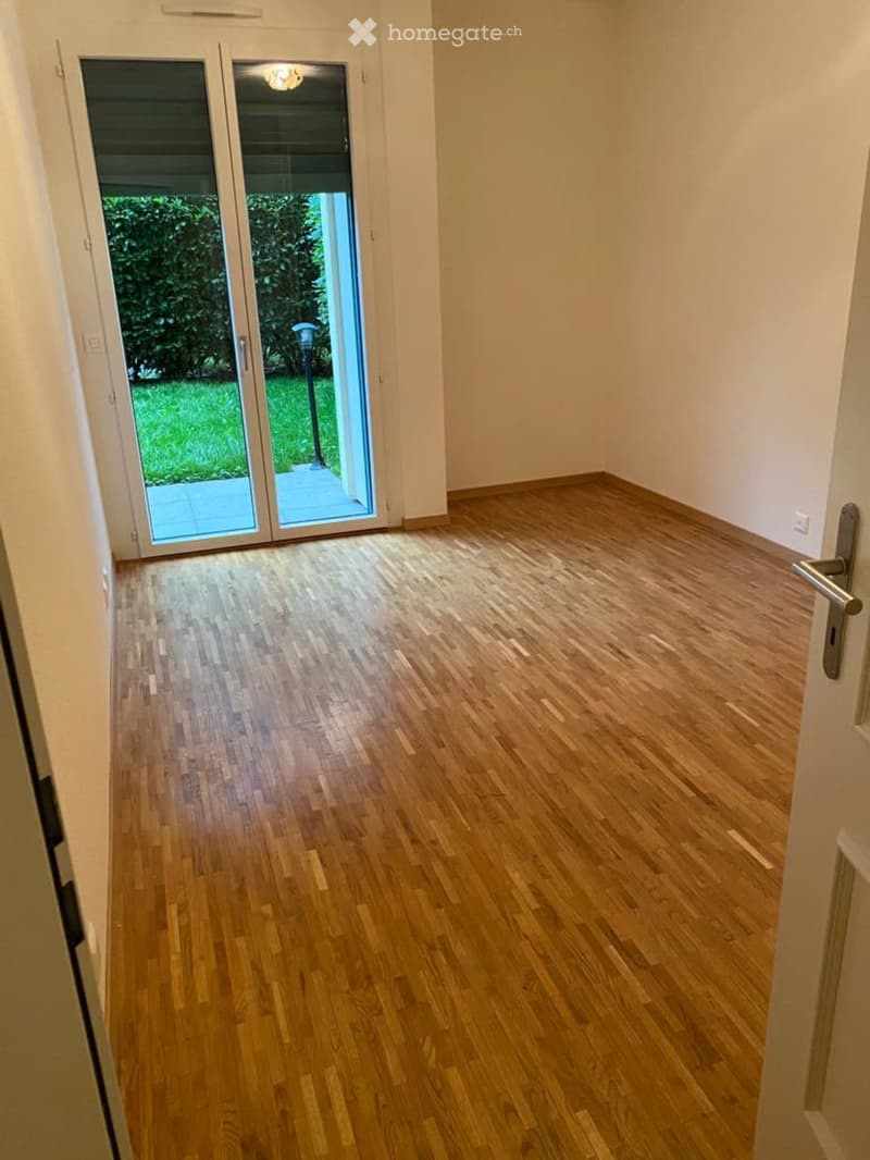 Empty room with wooden flooring, white walls, and a sliding glass door leading to a green outdoor area.