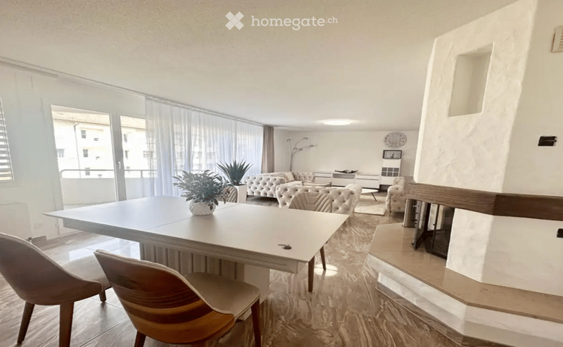Modern living room with a large window and balcony access, featuring a sofa, coffee table, chairs, a dining table, and a fireplace.