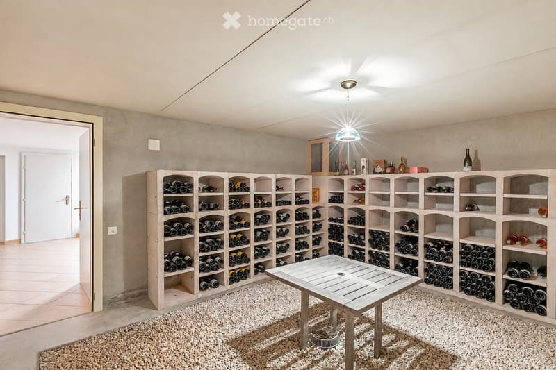 Wine cellar with wooden racks filled with wine bottles, a central wooden table, and a recessed ceiling light.