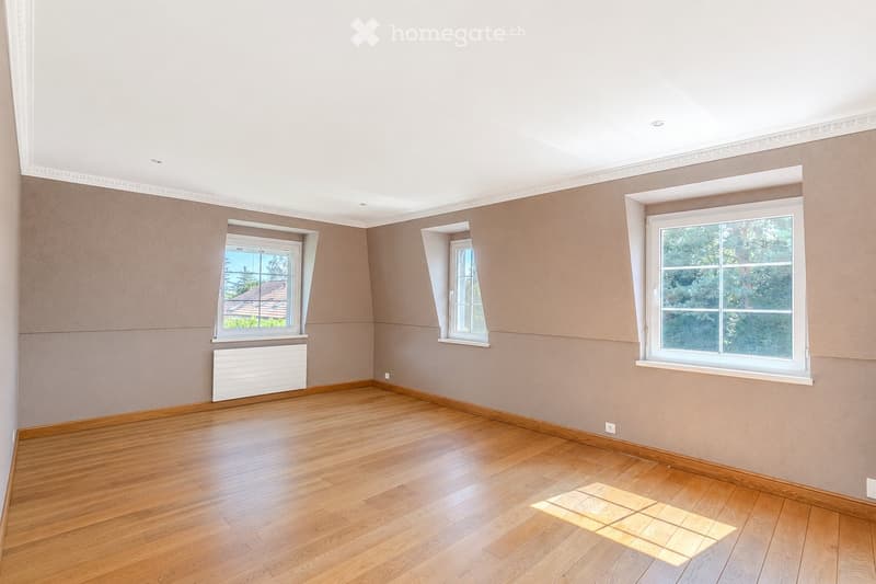 Empty room with wooden flooring, light-colored walls, and three windows offering natural light. A radiator is visible under one window.