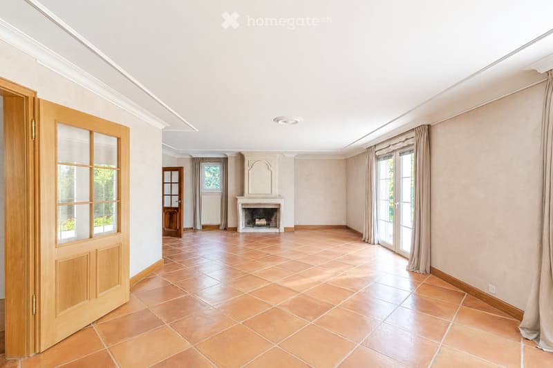 Empty room with beige tiled flooring, white walls, large windows with curtains, and a fireplace with a decorative mantel.