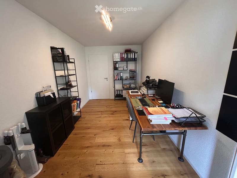 A well-organized office space with a wooden floor, a large desk with a computer setup, shelves filled with books and files, and a cabinet for storage.