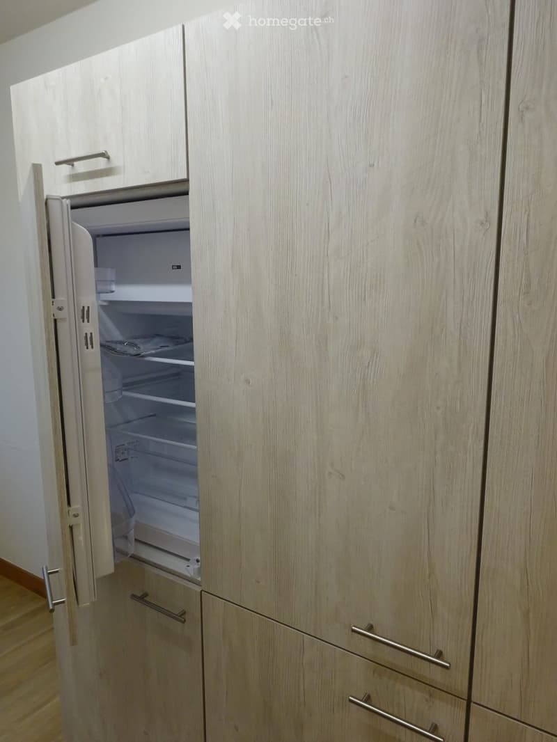 A modern kitchen with light wood cabinets and an open refrigerator showing its interior compartments.