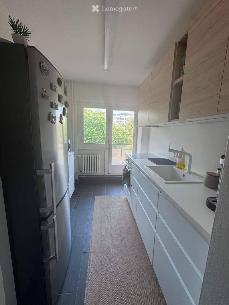 Modern kitchen with white cabinets, a stainless steel refrigerator, a sink with a modern faucet, and a window with a view of greenery.