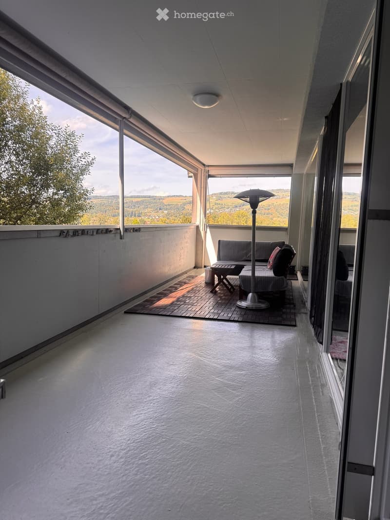 Balcony with a sofa, table, chair, and floor lamp, offering scenic views of the countryside.