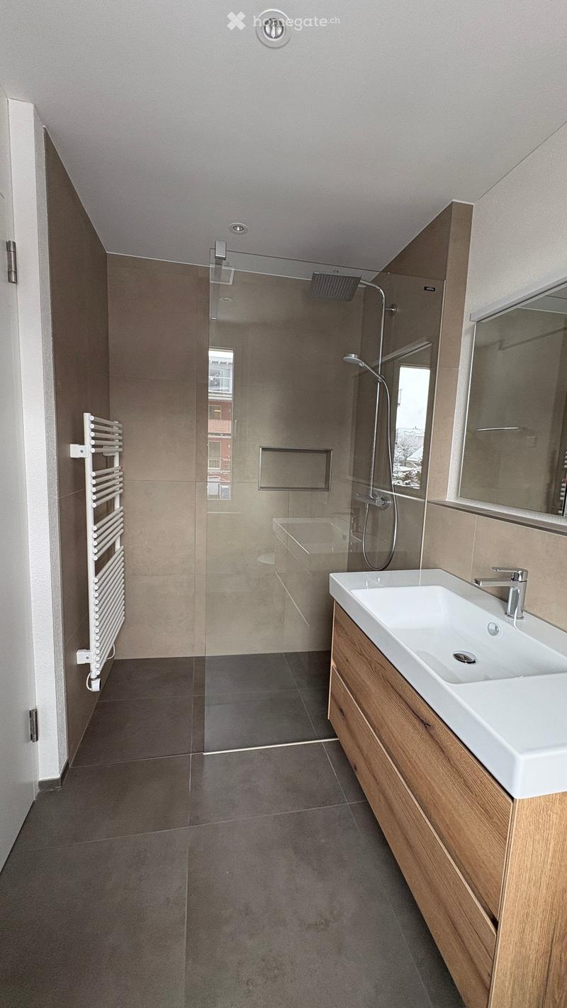 Modern bathroom with a white sink, wooden cabinet, large mirror, glass-enclosed shower, and a white radiator on the wall.