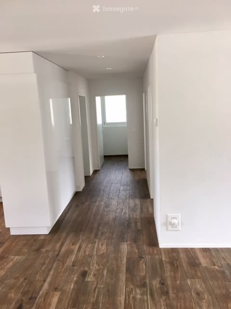 Empty hallway with wooden flooring and white walls, leading to a door at the end.