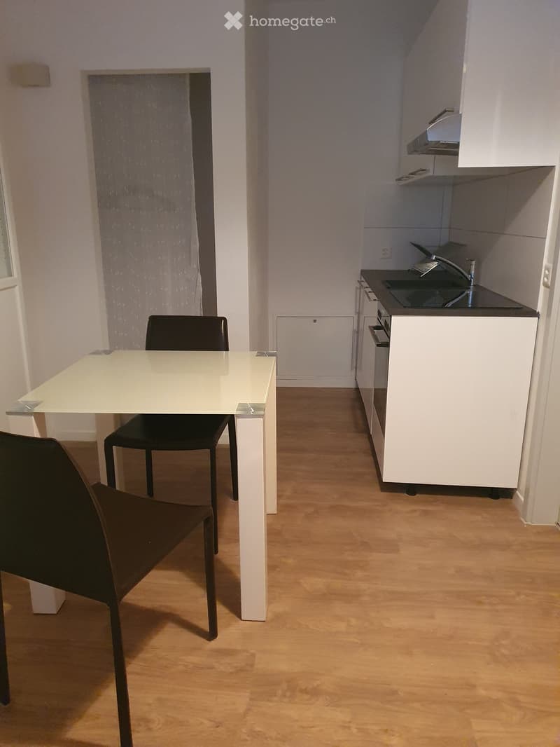 A modern, compact kitchen and dining area with white cabinets, a black countertop, a white dining table, and two black chairs.